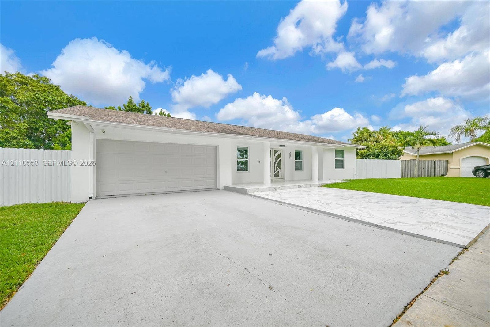 16611 SW 108th Court, Miami, FL 33157 Single-story exterior featuring white stucco siding, a tiled front patio, attached two-car garage, and perimeter privacy fencing