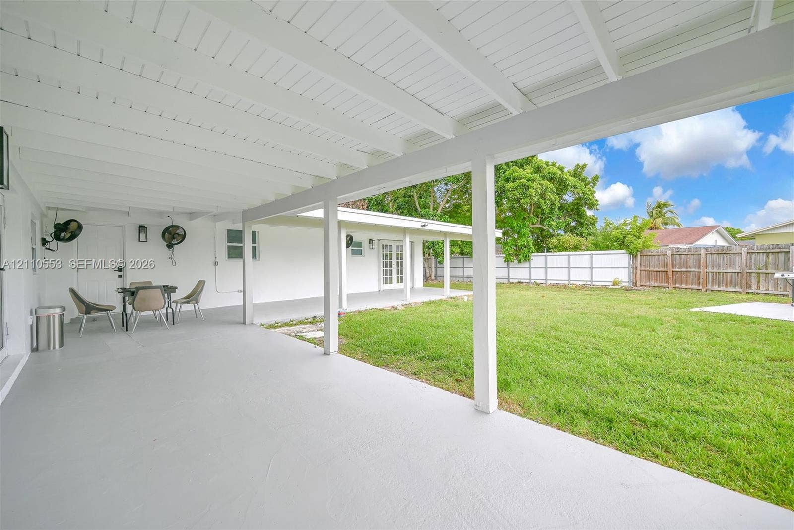 16611 SW 108th Court, Miami, FL 33157 Covered patio featuring white beamed ceilings, painted concrete flooring, and an expansive lawn enclosed by wood-panel fencing