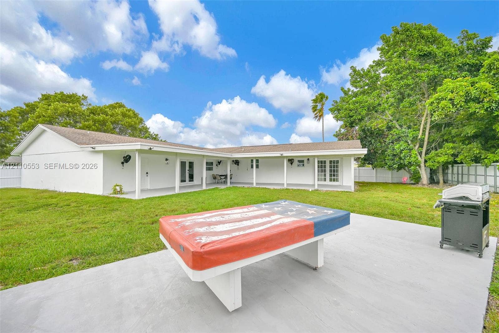 16611 SW 108th Court, Miami, FL 33157 Expansive backyard featuring a manicured lawn, concrete patio, covered porch, and perimeter privacy fencing