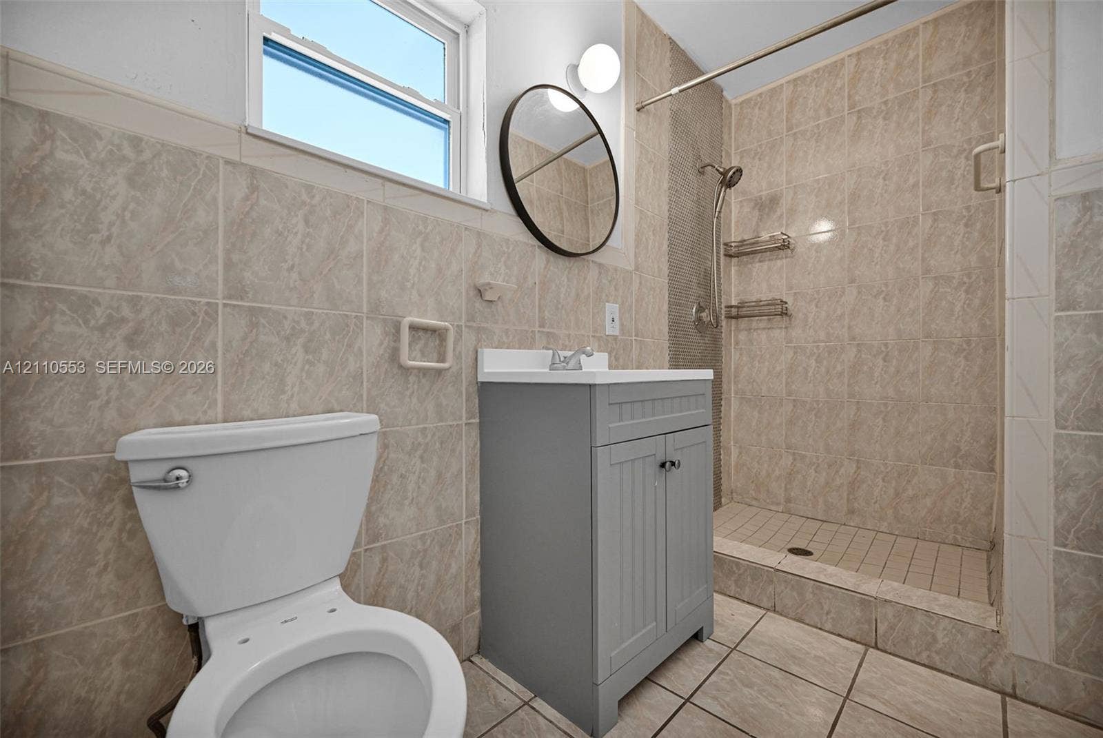 16611 SW 108th Court, Miami, FL 33157 Bathroom featuring tile-surround walk-in shower, grey shaker-style vanity with white countertop, round wall-mounted mirror, and tile flooring