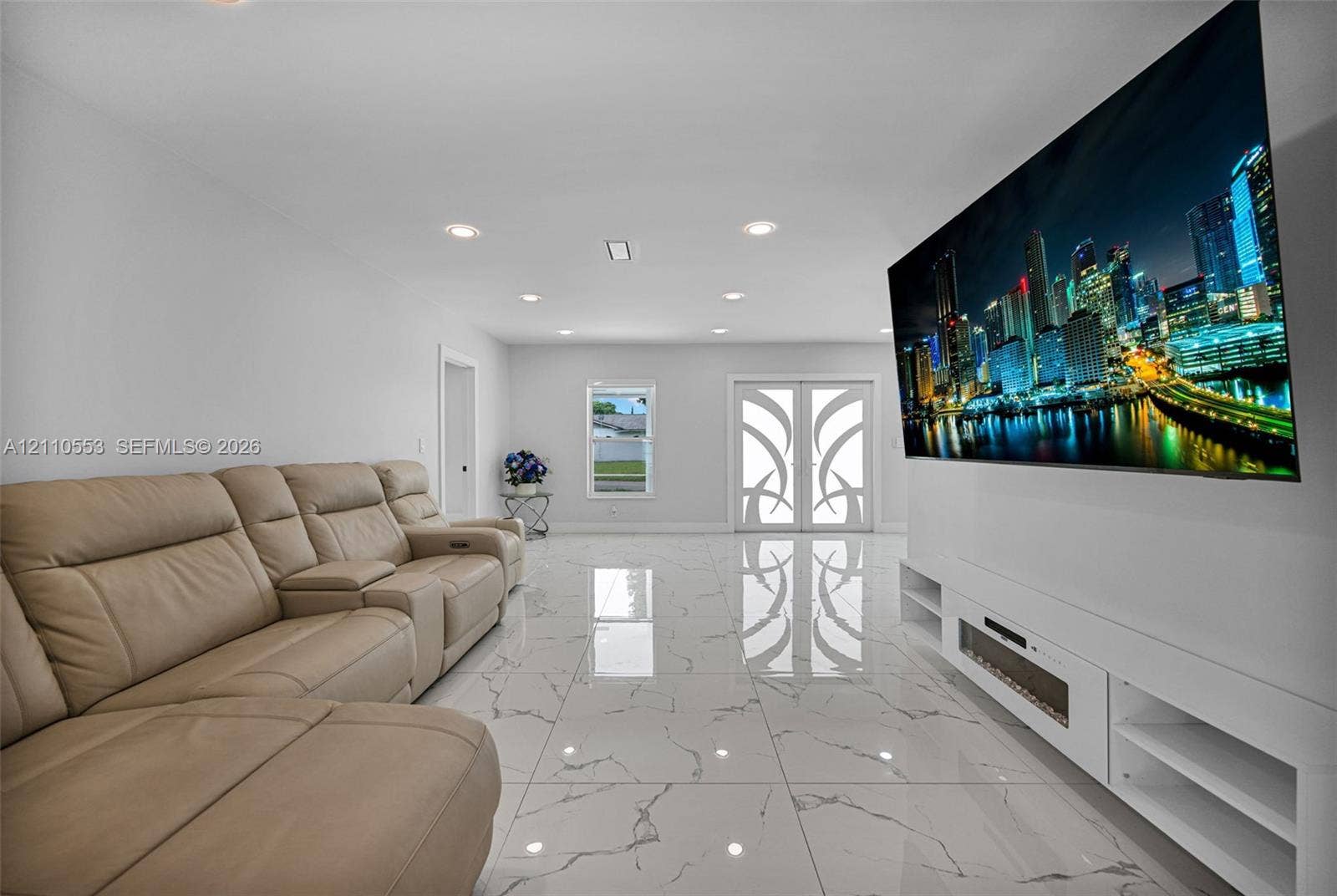 16611 SW 108th Court, Miami, FL 33157 Large-format tile flooring with marble-style veining, recessed lighting, double entry doors with decorative glass inserts, and a white built-in media console with an integrated electric fireplace
