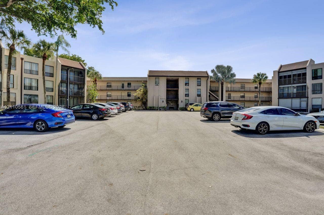 7950 W Mcnab Road, #222, Tamarac, FL 33321 Multi-story building exterior featuring paved surface parking and mature palm trees