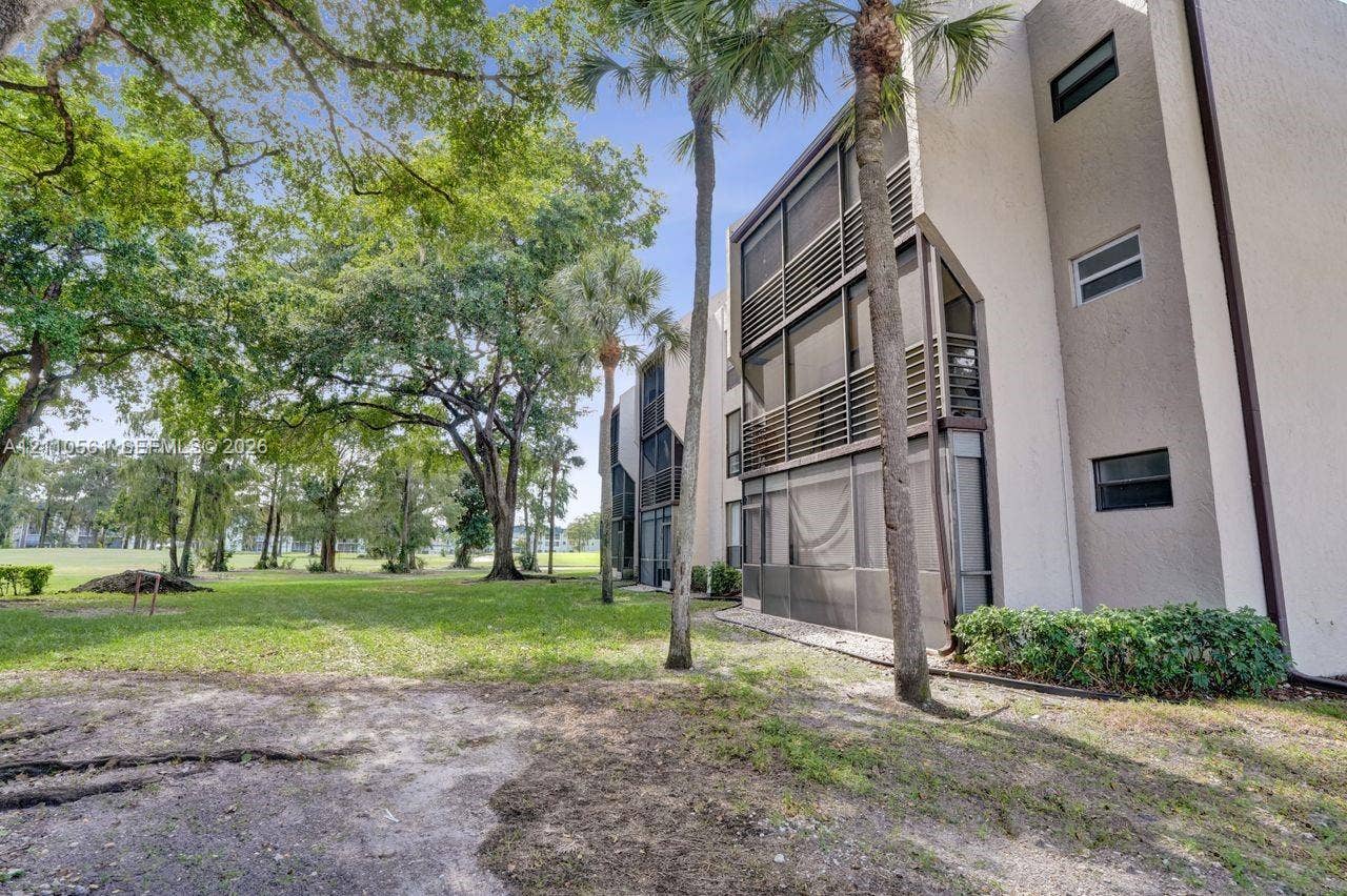 7950 W Mcnab Road, #222, Tamarac, FL 33321 Multi-story residential building exterior featuring stucco siding, multi-level screened-in balconies, and mature landscaping