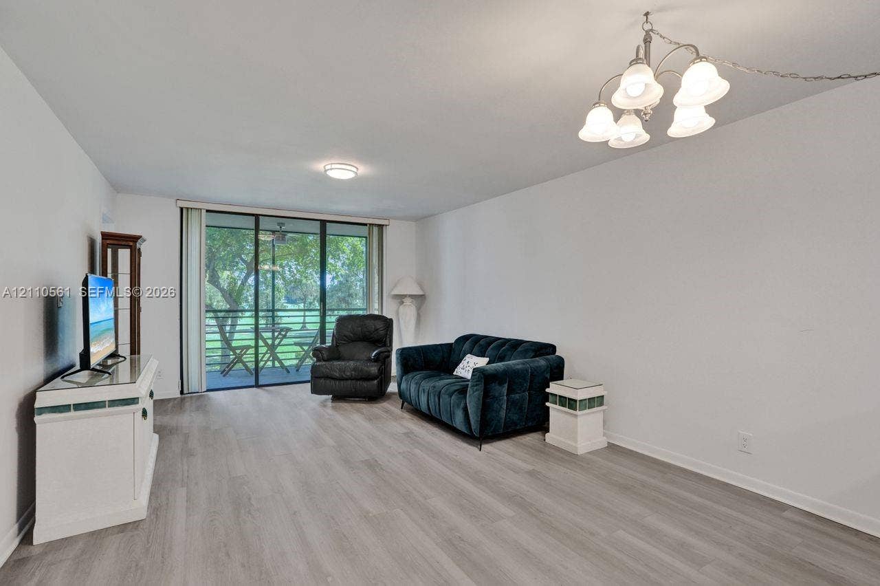 7950 W Mcnab Road, #222, Tamarac, FL 33321 Living area featuring wood-finish flooring, a multi-light chandelier, a ceiling-mounted light fixture, and sliding glass doors with screen enclosure