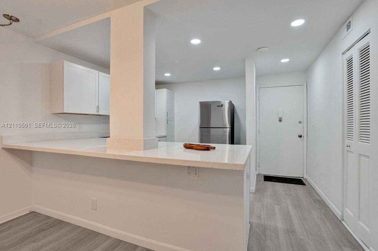 7950 W Mcnab Road, #222, Tamarac, FL 33321 Kitchen featuring a white peninsula with a solid-surface countertop, flat-panel white cabinetry, recessed lighting, wood-finish flooring, and stainless steel refrigerator