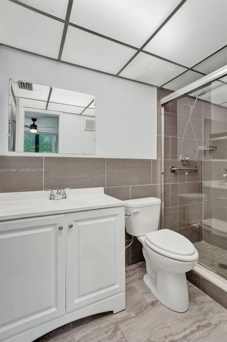 7950 W Mcnab Road, #222, Tamarac, FL 33321 Bathroom featuring a white vanity cabinet, solid-surface countertop, walk-in shower with tiled walls, and drop ceiling panel lighting