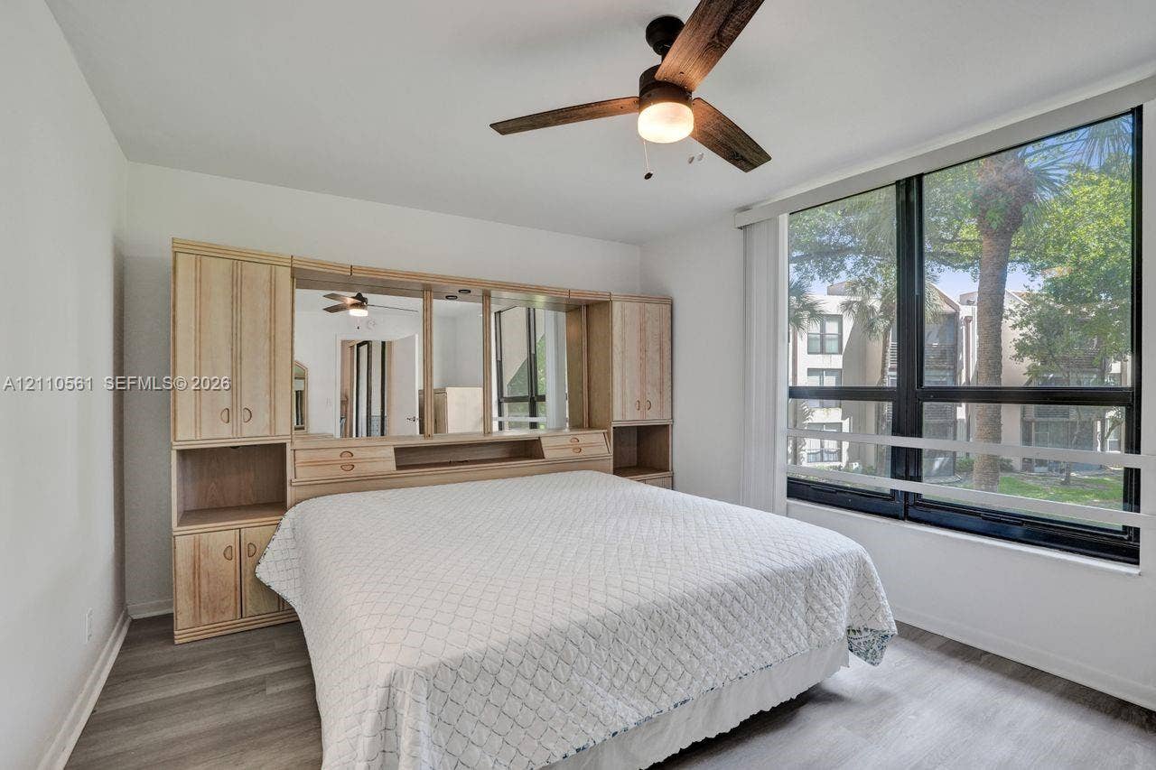 7950 W Mcnab Road, #222, Tamarac, FL 33321 Room featuring wood-finish flooring, built-in light-colored cabinetry with integrated shelving and mirrored accents, and floor-to-ceiling windows with horizontal mullions, complemented by a ceiling fan with light fixture