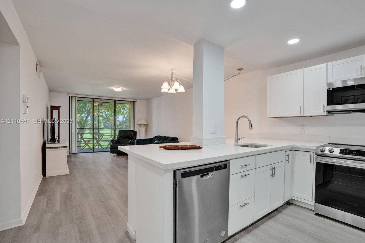 7950 W Mcnab Road, #222, Tamarac, FL 33321 Kitchen featuring white cabinetry, solid surface countertops, stainless steel appliances, and wood-finish flooring