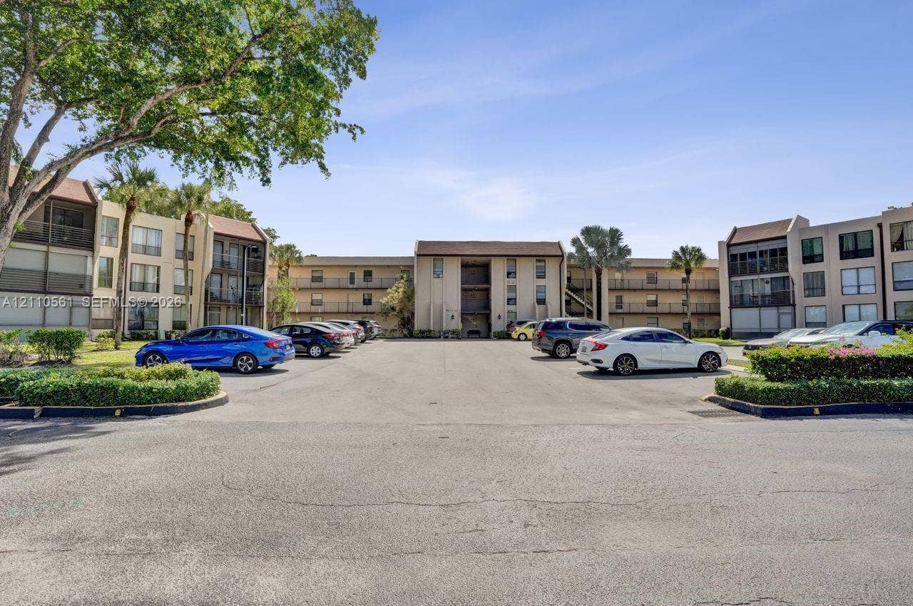 7950 W Mcnab Road, #222, Tamarac, FL 33321 Multi-story exterior featuring a neutral stucco facade, shingled roofing, integrated balconies, and mature landscaping