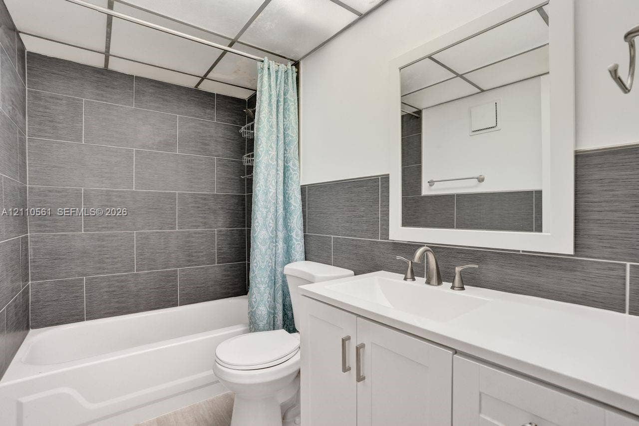 7950 W Mcnab Road, #222, Tamarac, FL 33321 Bathroom featuring a white vanity cabinet with a solid surface countertop, an undermount sink, brushed nickel hardware, and grey textured tile surround in the shower area