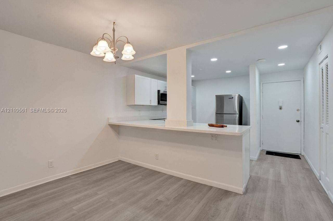7950 W Mcnab Road, #222, Tamarac, FL 33321 Kitchen featuring a peninsula with solid-surface countertop, white cabinetry, stainless steel refrigerator, recessed lighting, and wood-finish flooring