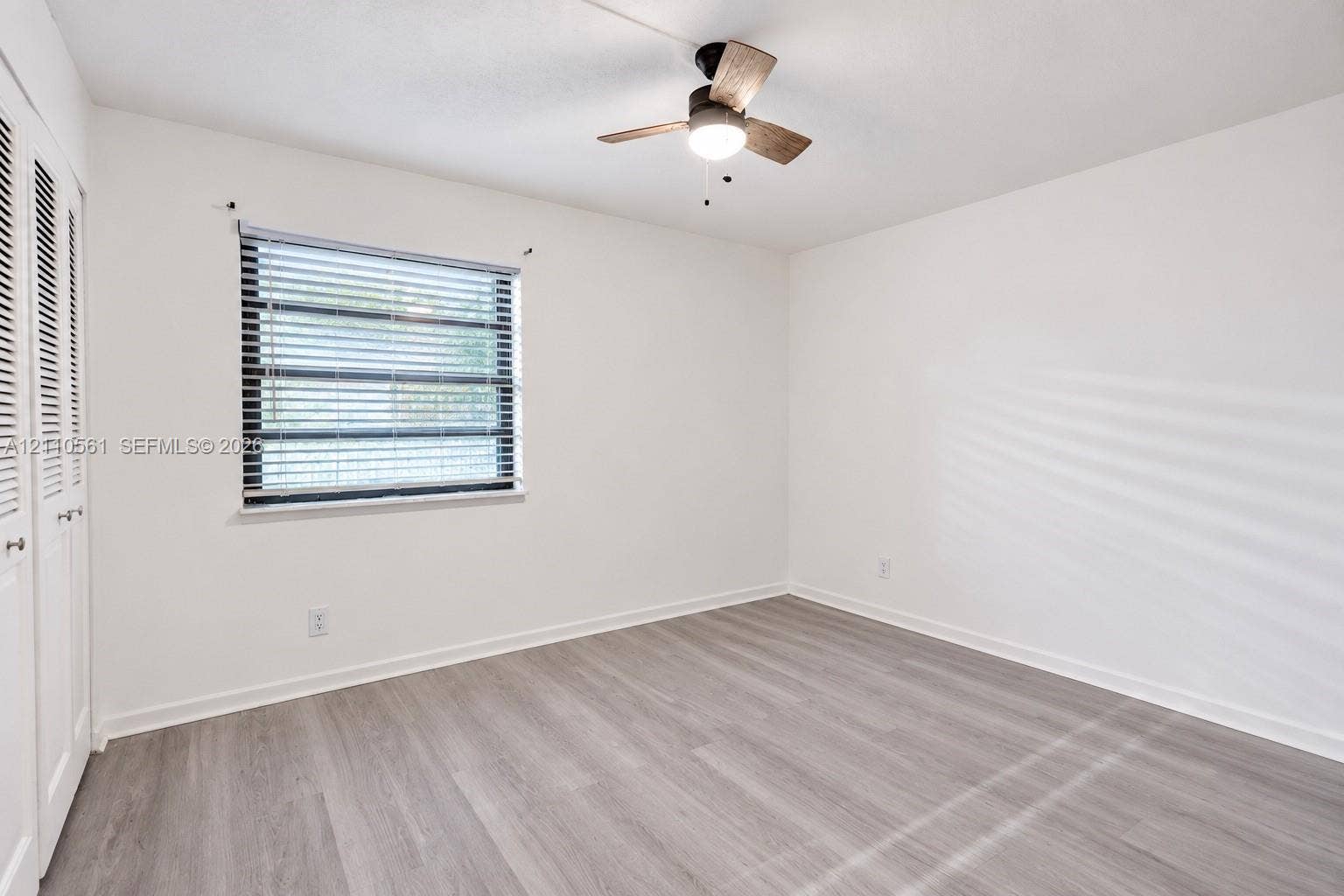 7950 W Mcnab Road, #222, Tamarac, FL 33321 Neutral-toned wood-finish flooring, ceiling fan with integrated lighting, window with horizontal blinds, and double-door closet with louvered panels