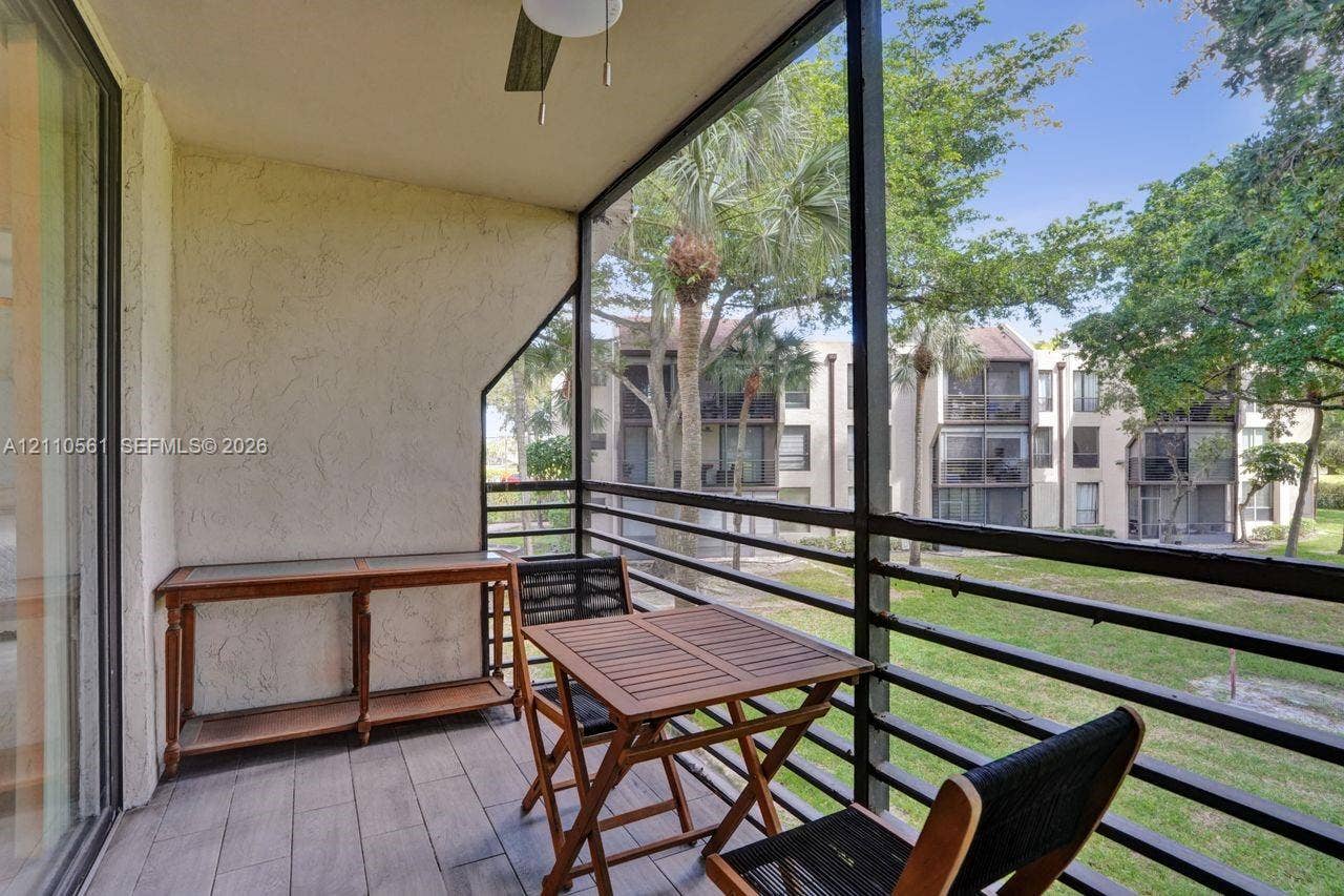 7950 W Mcnab Road, #222, Tamarac, FL 33321 Screened balcony featuring tile flooring, textured stucco walls, black metal railing, and a ceiling fan
