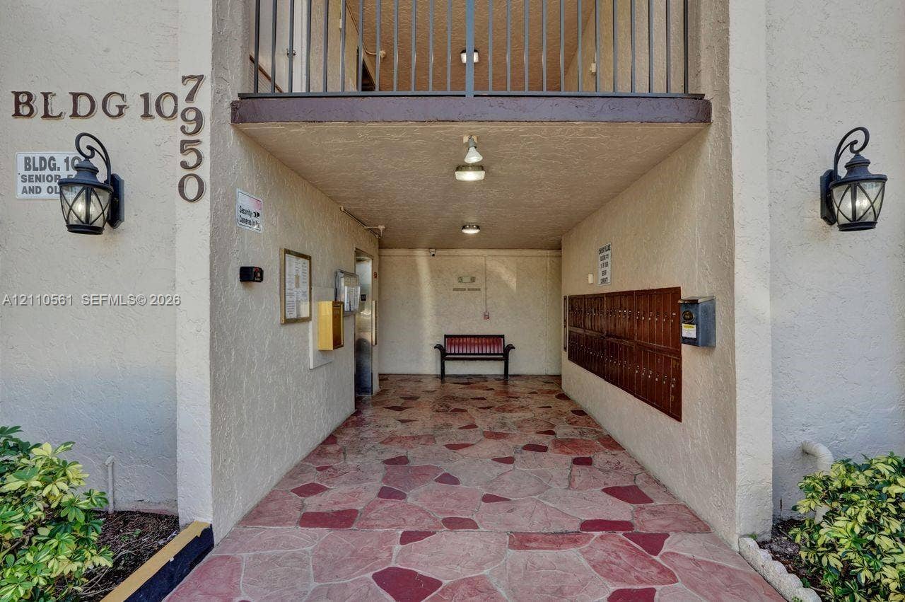 7950 W Mcnab Road, #222, Tamarac, FL 33321 Covered building entrance featuring flagstone-style paving, wall-mounted carriage-style light fixtures, and integrated mailboxes