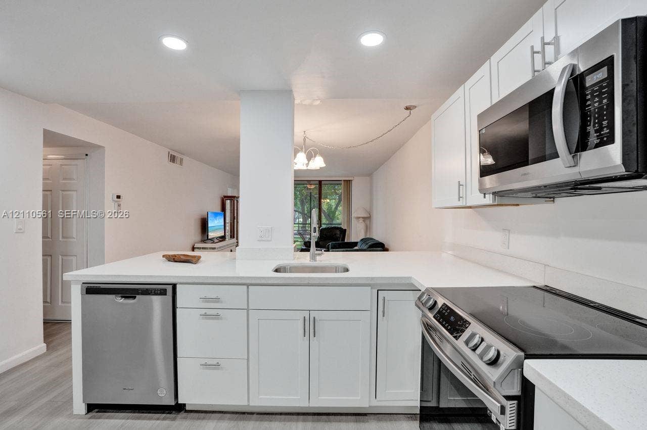 7950 W Mcnab Road, #222, Tamarac, FL 33321 Kitchen featuring white cabinetry, solid-surface countertops, recessed lighting, and stainless steel appliances, including an over-the-range microwave, dishwasher, and electric range
