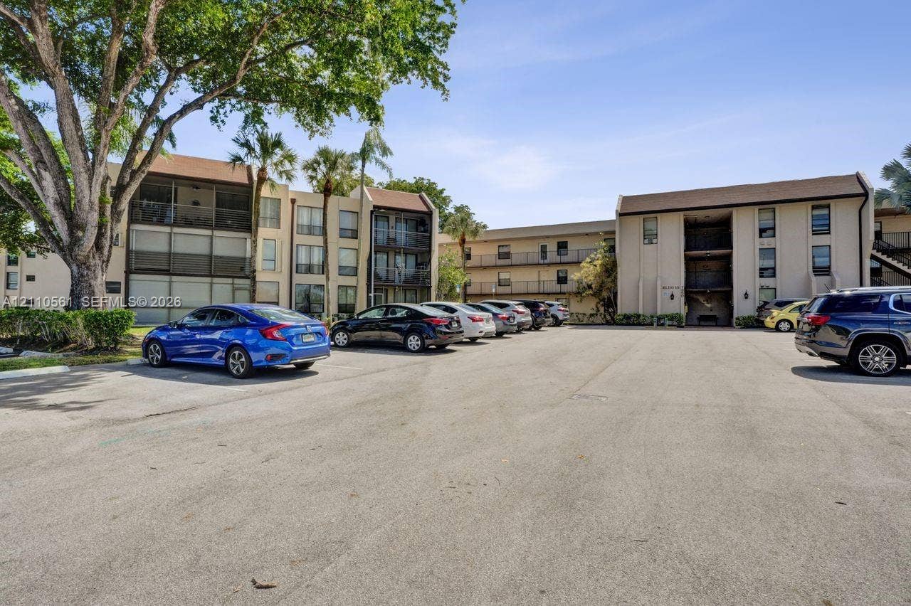 7950 W Mcnab Road, #222, Tamarac, FL 33321 Multi-story complex exterior featuring neutral stucco siding, pitched roofs, screen-enclosed balconies, and mature landscaping