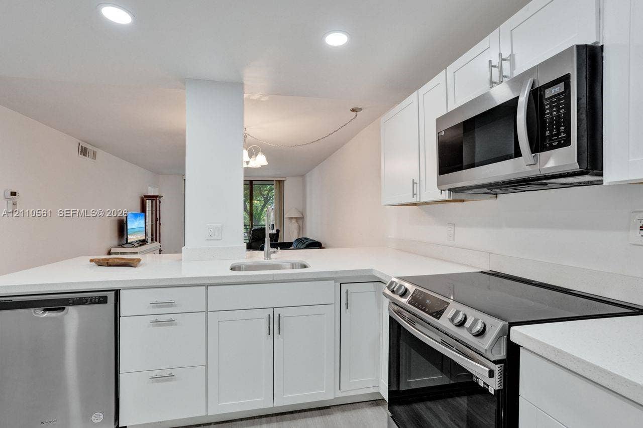 7950 W Mcnab Road, #222, Tamarac, FL 33321 Kitchen featuring white cabinetry, solid-surface countertops, recessed ceiling lighting, and stainless steel appliances including a microwave, dishwasher, and range