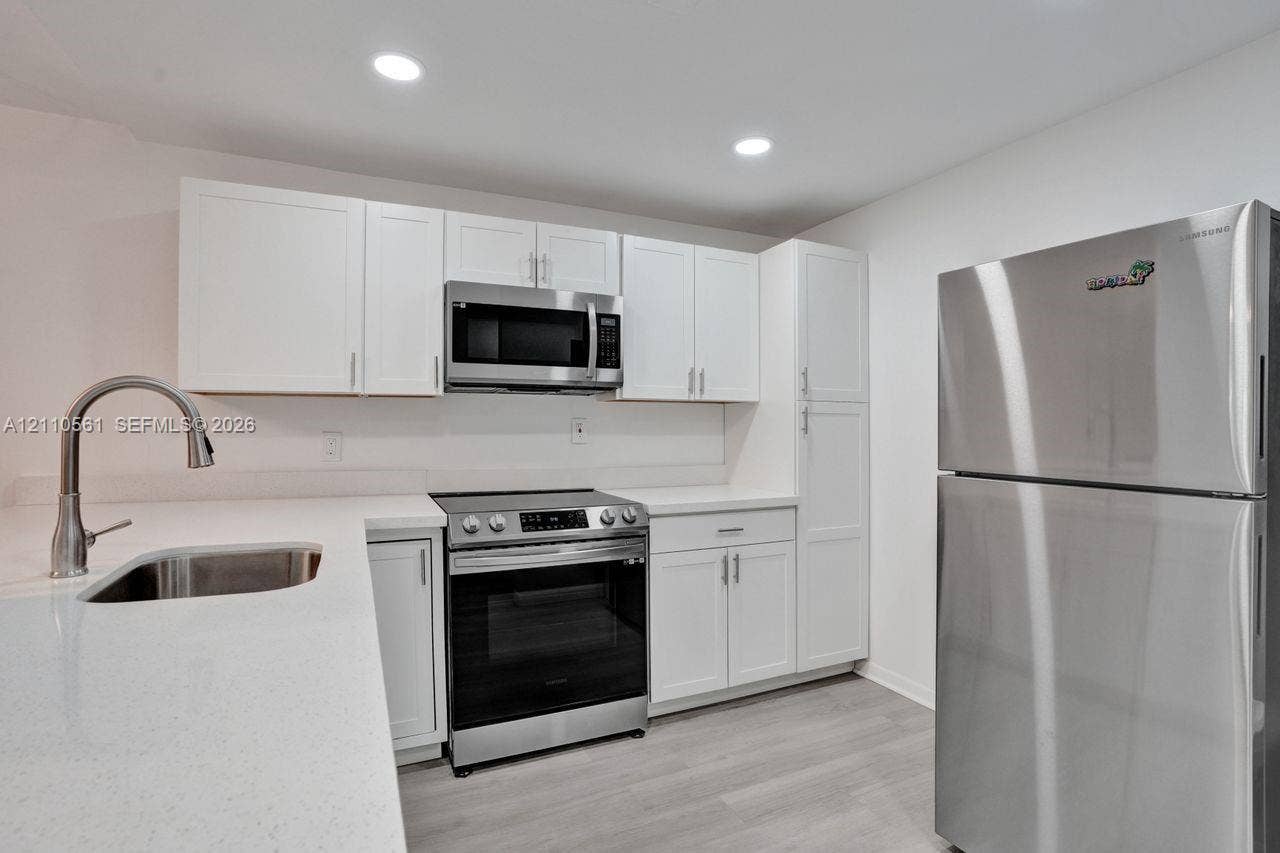 7950 W Mcnab Road, #222, Tamarac, FL 33321 Kitchen featuring white shaker-style cabinetry, solid-surface countertops, recessed lighting, wood-finish flooring, and stainless steel appliances