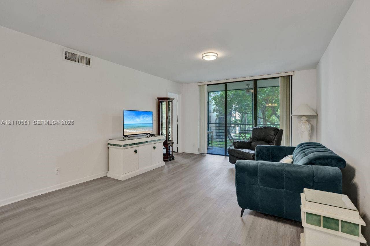 7950 W Mcnab Road, #222, Tamarac, FL 33321 Living area featuring neutral wall paint, wood-finish flooring, a central flush-mount ceiling light, and large sliding glass doors providing outdoor access