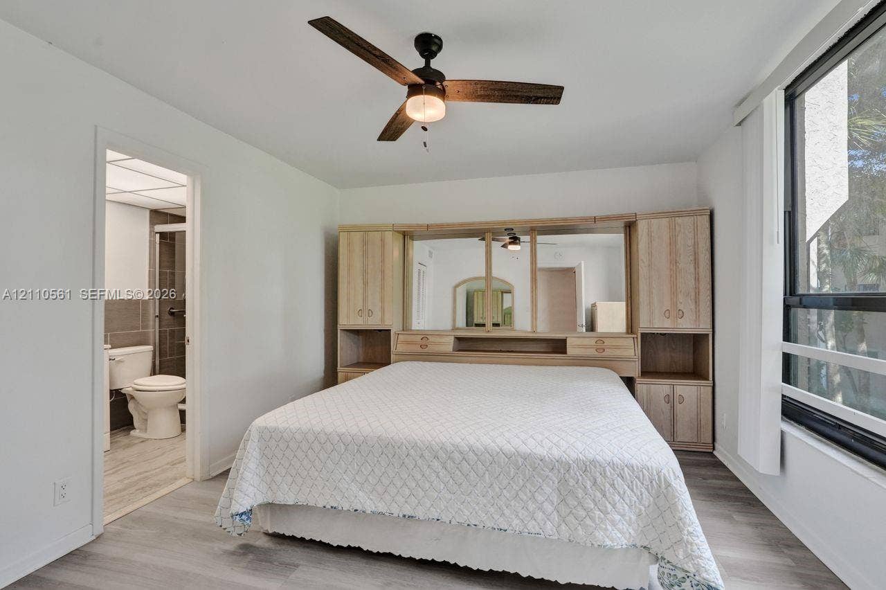 7950 W Mcnab Road, #222, Tamarac, FL 33321 Room featuring light wood-finish flooring, a ceiling fan with integrated lighting, a large window, and built-in wood cabinetry with central mirrored panels