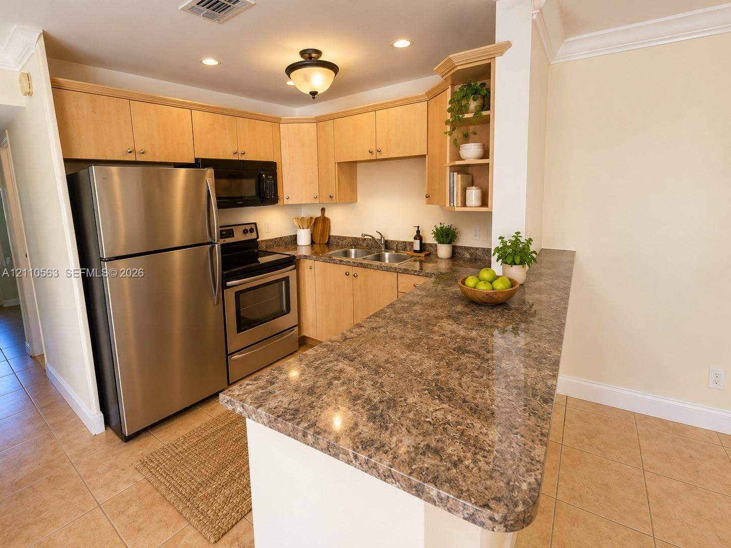 Kitchen featuring wood cabinetry, stainless steel appliances, a peninsula with stone-finish countertops, ceramic tile flooring, and recessed lighting