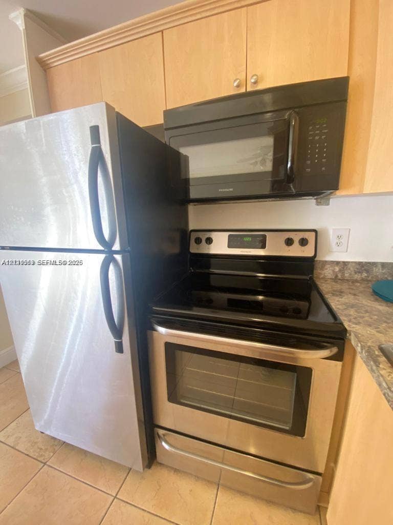 Kitchen featuring natural wood-finish cabinetry, stainless steel refrigerator, electric range with matching microwave, and stone-patterned countertops