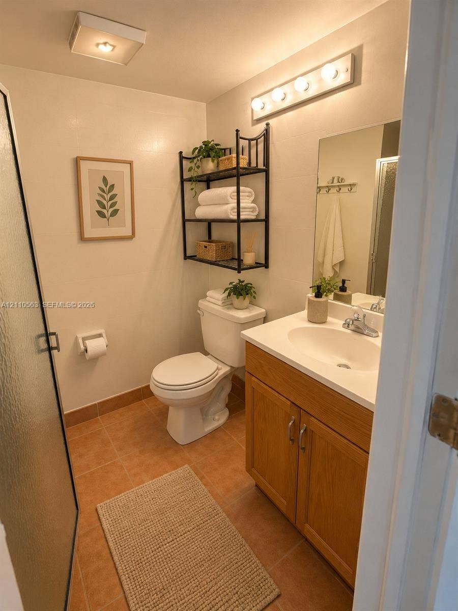 Bathroom featuring wood-finish vanity cabinetry with an integrated sink, tiled flooring, wall-mounted light fixture, and walk-in shower with a glass door