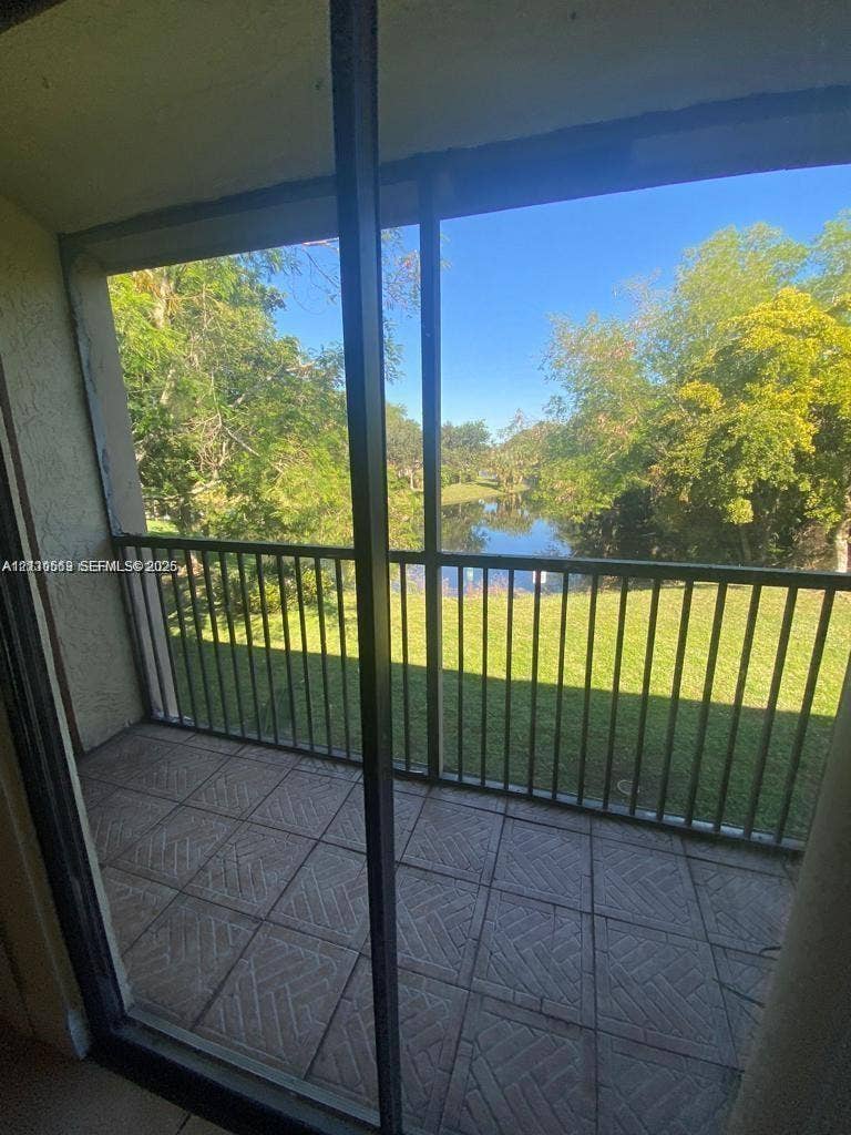 Screened-in balcony featuring ceramic tile flooring, a metal railing, and a backdrop of mature trees and water