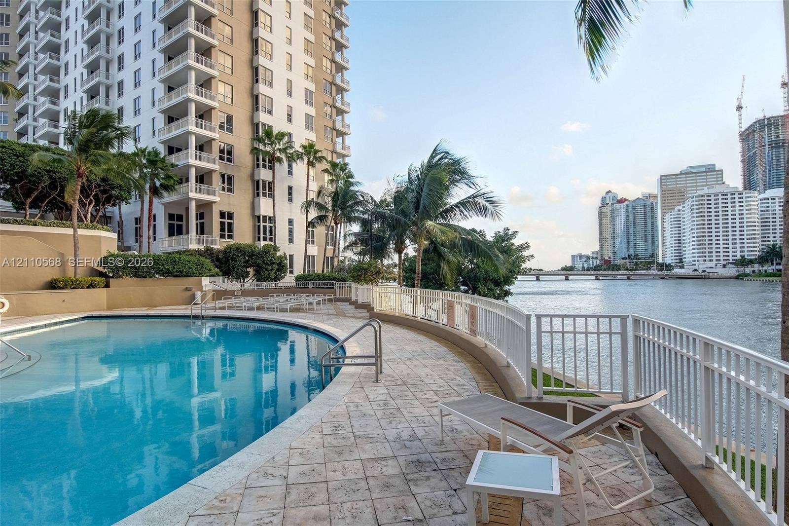 801 Brickell Key Boulevard, #2006, Miami, FL 33131 Curved swimming pool with stone-tiled deck, white metal perimeter fencing, and palms overlooking the waterway