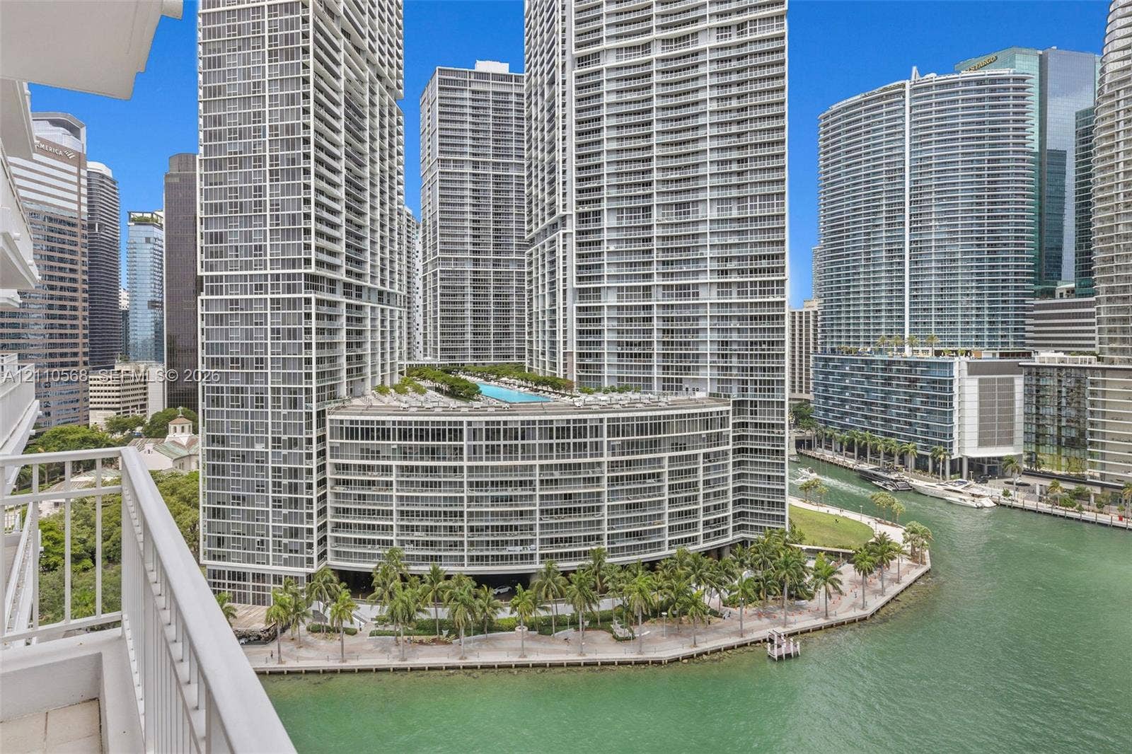 801 Brickell Key Boulevard, #2006, Miami, FL 33131 High-rise balcony with white metal railing overlooking a waterfront promenade, palm tree landscaping, and a multi-level complex featuring an elevated swimming pool