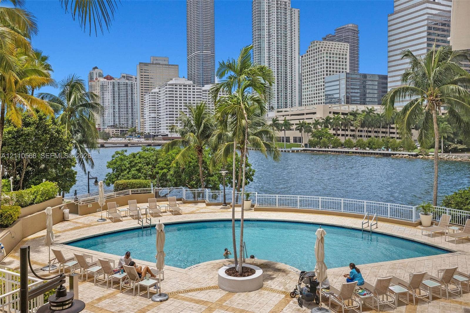 801 Brickell Key Boulevard, #2006, Miami, FL 33131 Curved swimming pool featuring stone paver decking, integrated central palm tree planter, and white picket-style perimeter fencing