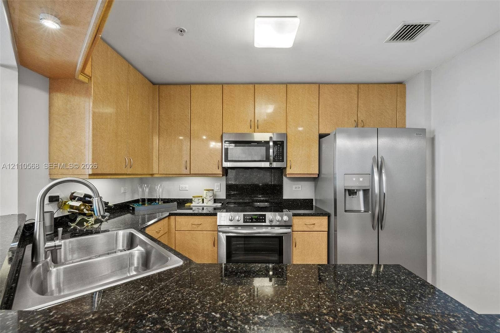 801 Brickell Key Boulevard, #2006, Miami, FL 33131 Kitchen featuring light-finish wood cabinetry, dark stone countertops, stainless steel appliances, and a double-basin undermount sink with a gooseneck faucet