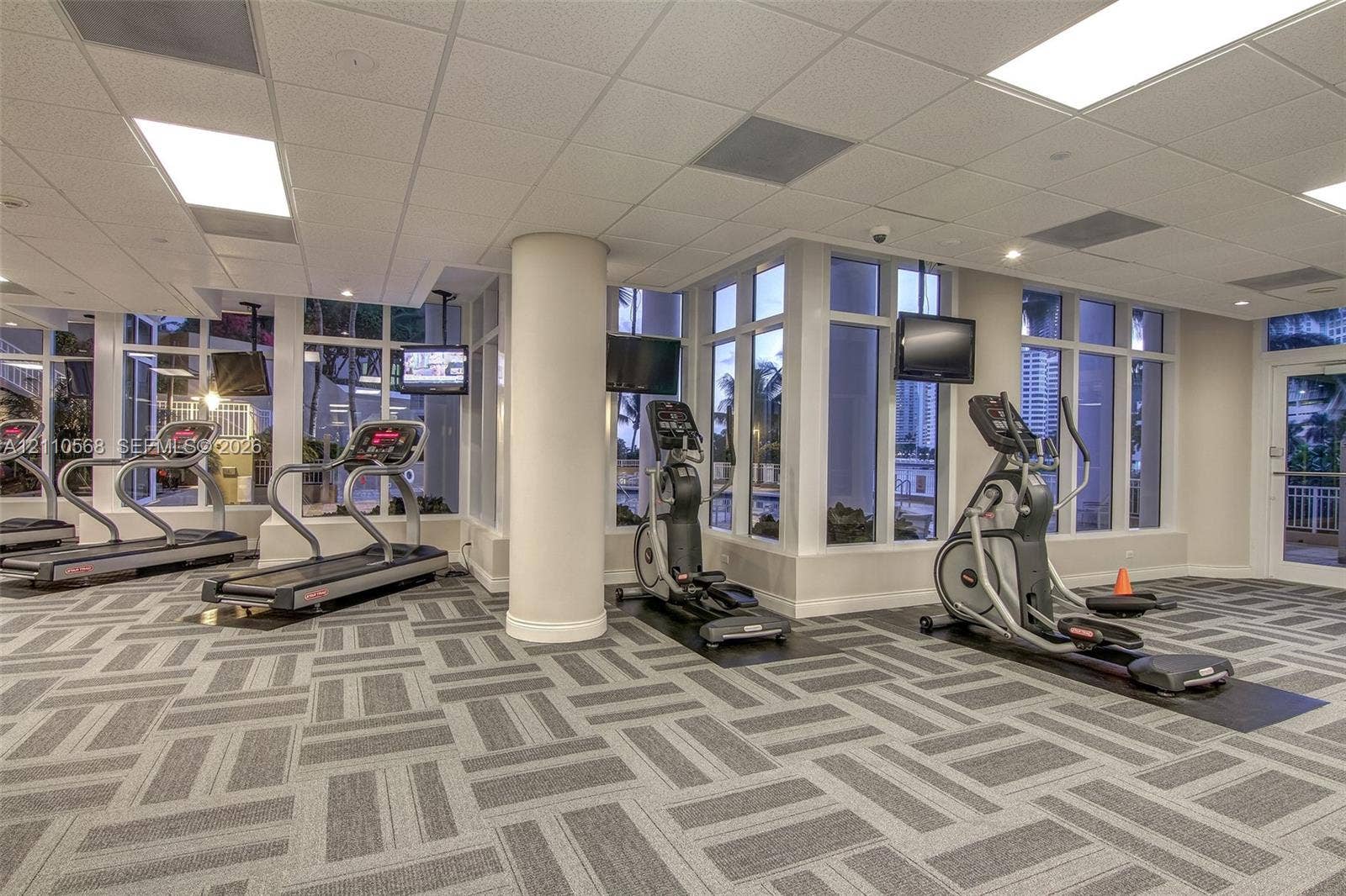 801 Brickell Key Boulevard, #2006, Miami, FL 33131 Fitness center featuring expansive floor-to-ceiling windows, high-contrast patterned commercial carpeting, recessed lighting, and structural support columns