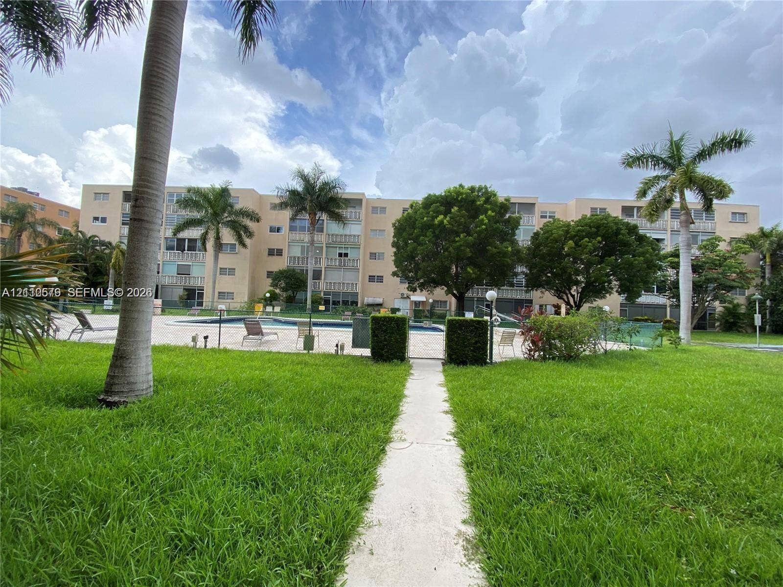 232 NE 12th Avenue, #301, Hallandale Beach, FL 33009 Ground-level recreational area featuring a paved walkway, swimming pool, manicured lawn, mature palm trees, and professional landscaping