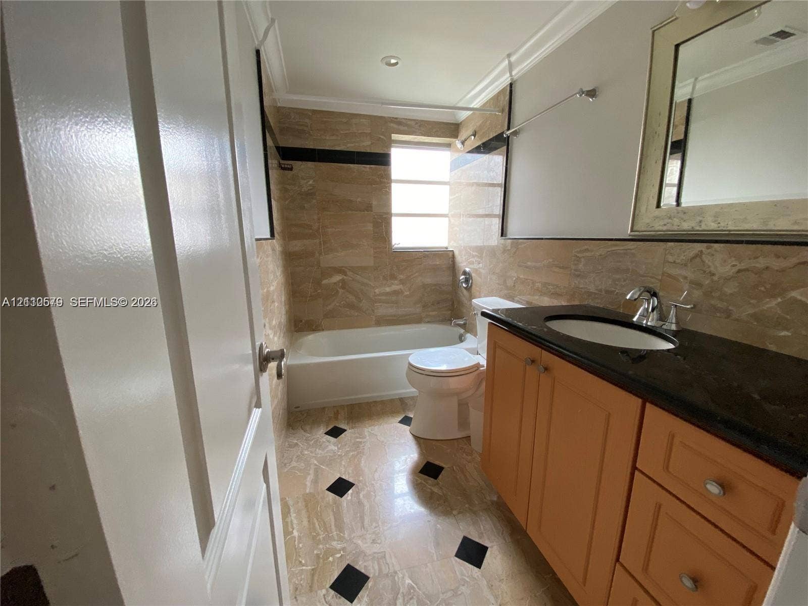 232 NE 12th Avenue, #301, Hallandale Beach, FL 33009 Bathroom featuring stone tile flooring with decorative black insets, a vanity with a dark countertop and integrated sink, stone-tiled wall surrounds, and a porcelain soaking tub