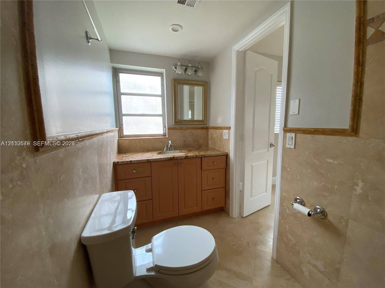 232 NE 12th Avenue, #301, Hallandale Beach, FL 33009 Bathroom featuring stone-tile wall wainscoting, wood-finish cabinetry, natural stone countertop, undermount sink, and wall-mounted vanity mirror