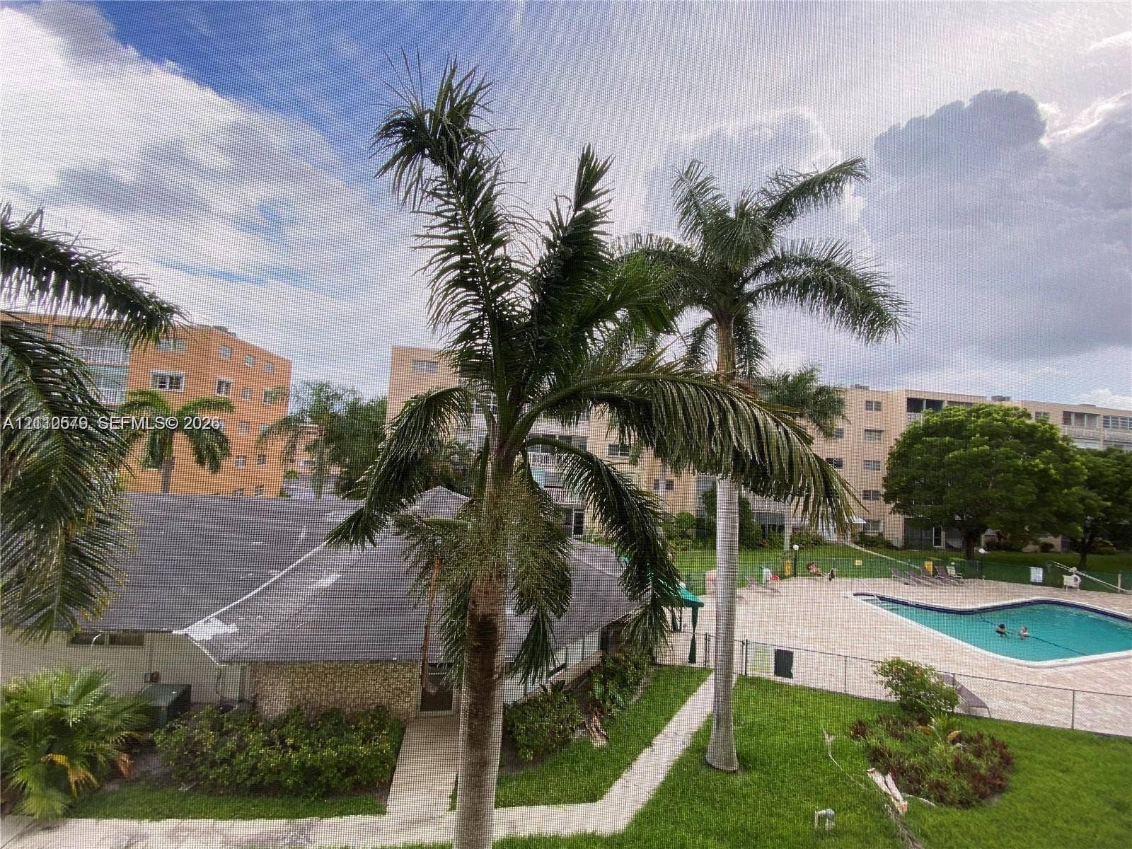 232 NE 12th Avenue, #301, Hallandale Beach, FL 33009 Outdoor community swimming pool with fenced perimeter, manicured green space, and mature palm tree landscaping