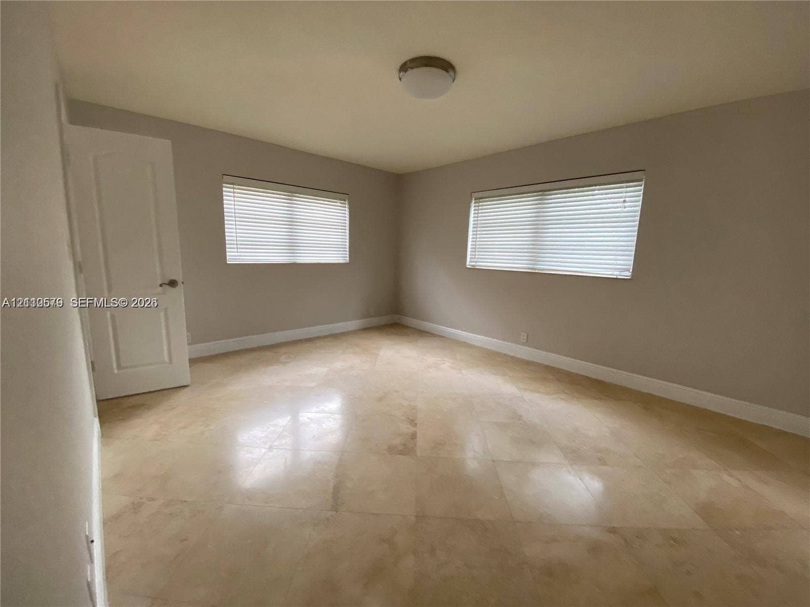232 NE 12th Avenue, #301, Hallandale Beach, FL 33009 Interior room featuring large-format tile flooring, neutral wall paint, two windows with horizontal blinds, and a paneled interior door