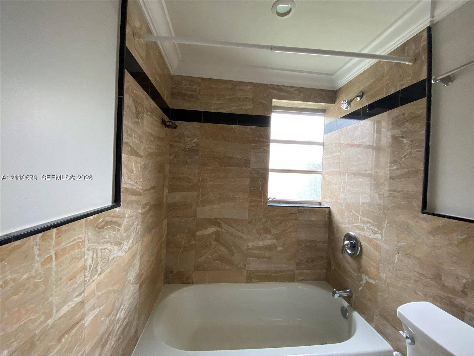 232 NE 12th Avenue, #301, Hallandale Beach, FL 33009 Full-height natural-tone stone wall tiling with contrasting black accent trim, integrated bathtub, and polished metal shower fixtures