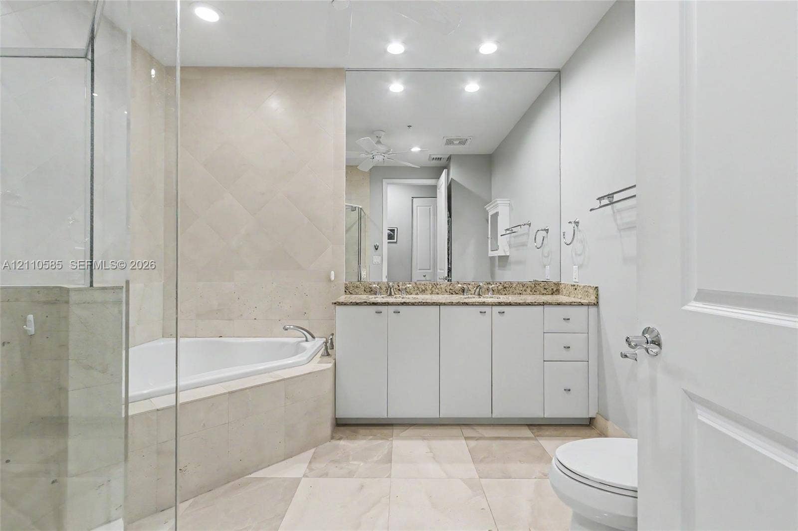 600 W Las Olas Boulevard, #202S, Fort Lauderdale, FL 33312 Main Bathroom featuring a double-sink vanity with stone countertop, corner soaking tub with tile surround, glass-enclosed shower, and large wall-mounted mirror