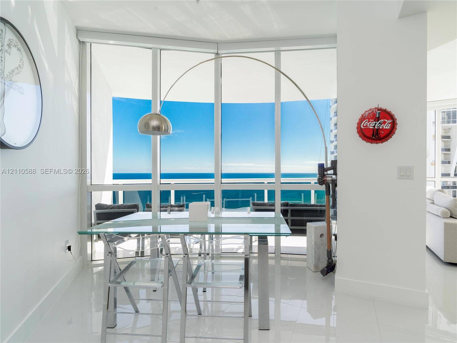 Floor-to-ceiling glass windows, polished tile flooring, and a glass-paneled balcony railing with expansive ocean exposure