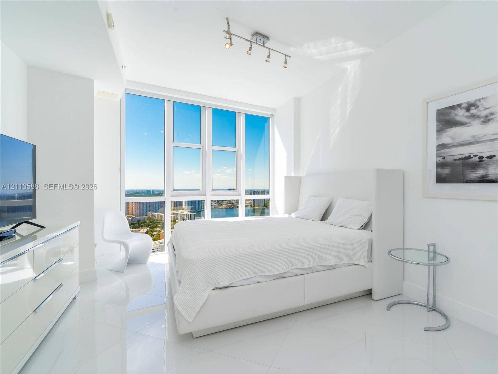 Floor-to-ceiling windows featuring panoramic urban and water scenery, polished stone tile flooring, and adjustable track lighting