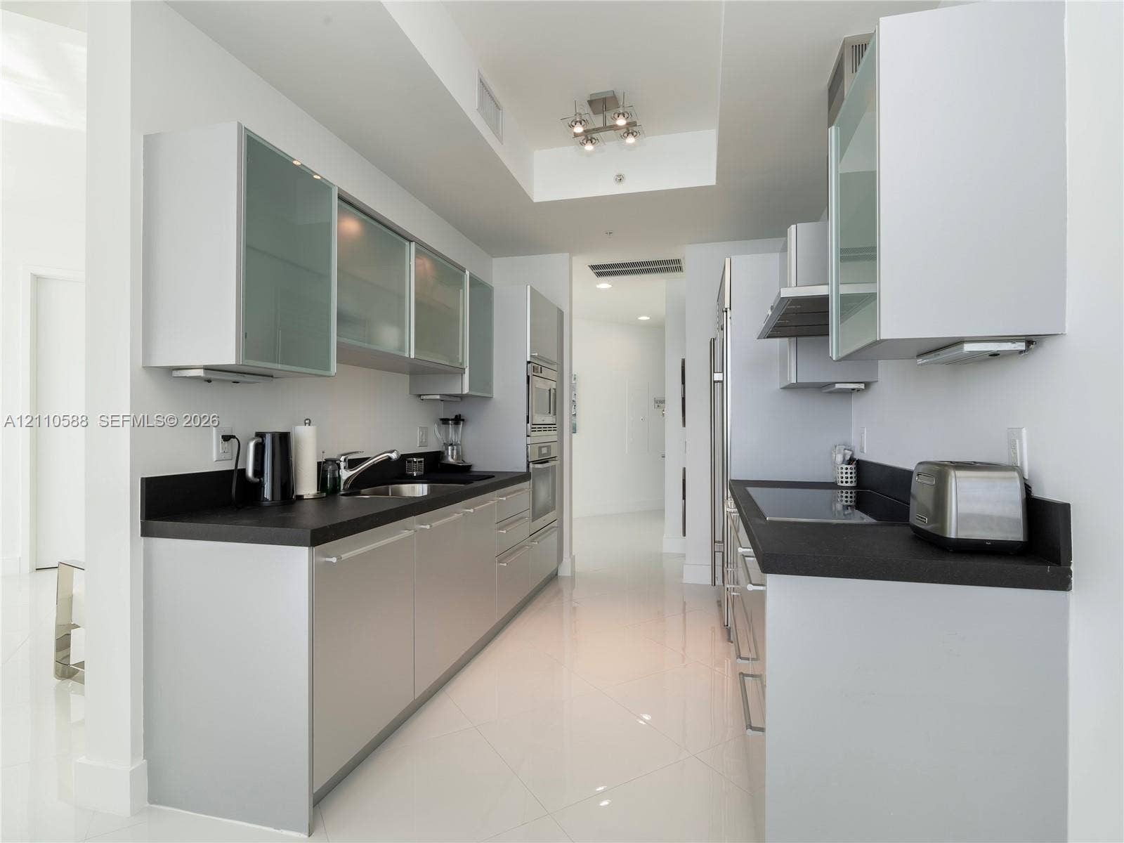Contemporary kitchen featuring flat-panel cabinetry, frosted glass-front upper cabinets, contrasting dark countertops, integrated stainless steel appliances, and polished tile flooring