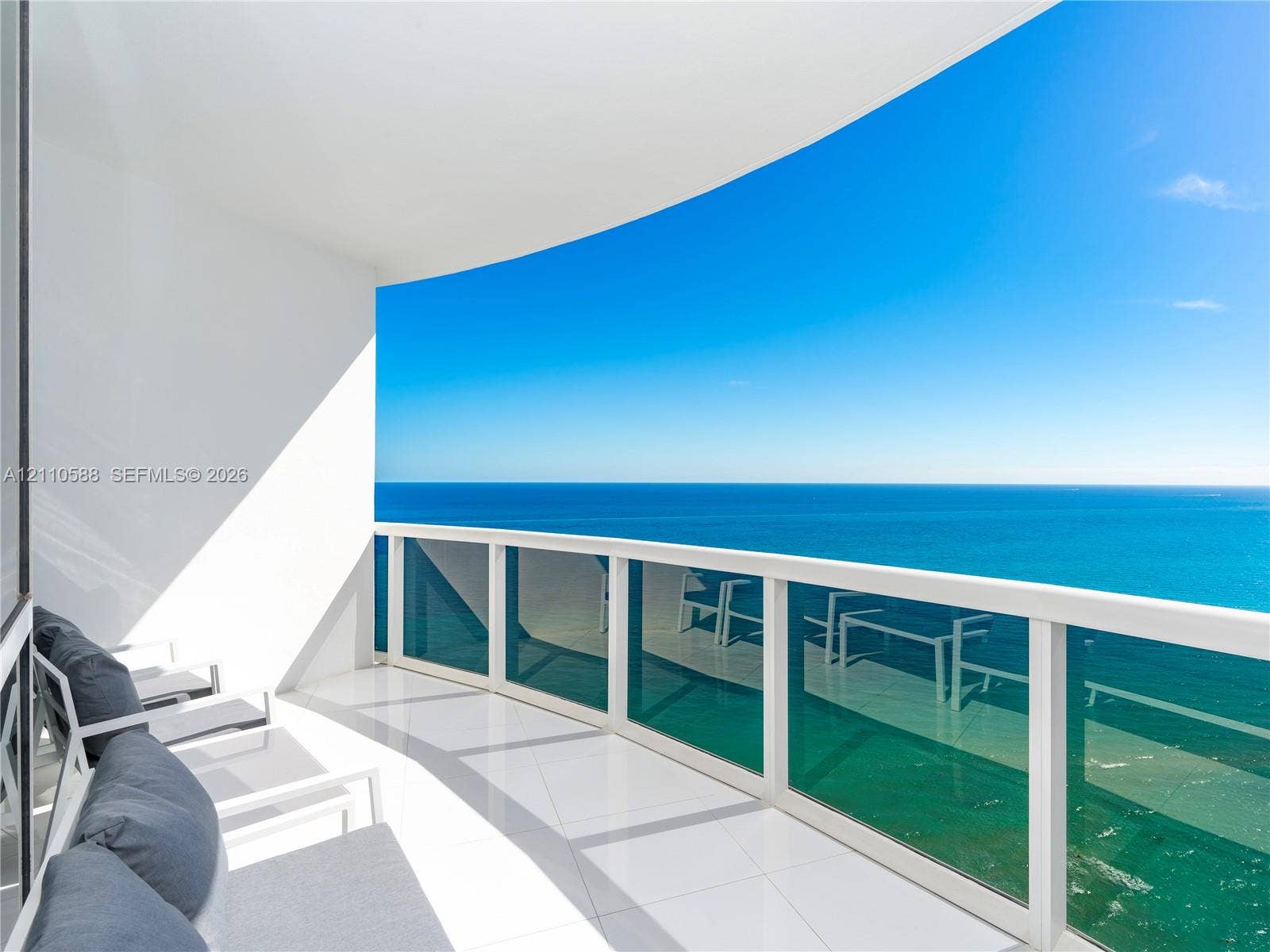 Covered balcony featuring white tiled flooring and a glass panel railing with an expansive ocean horizon