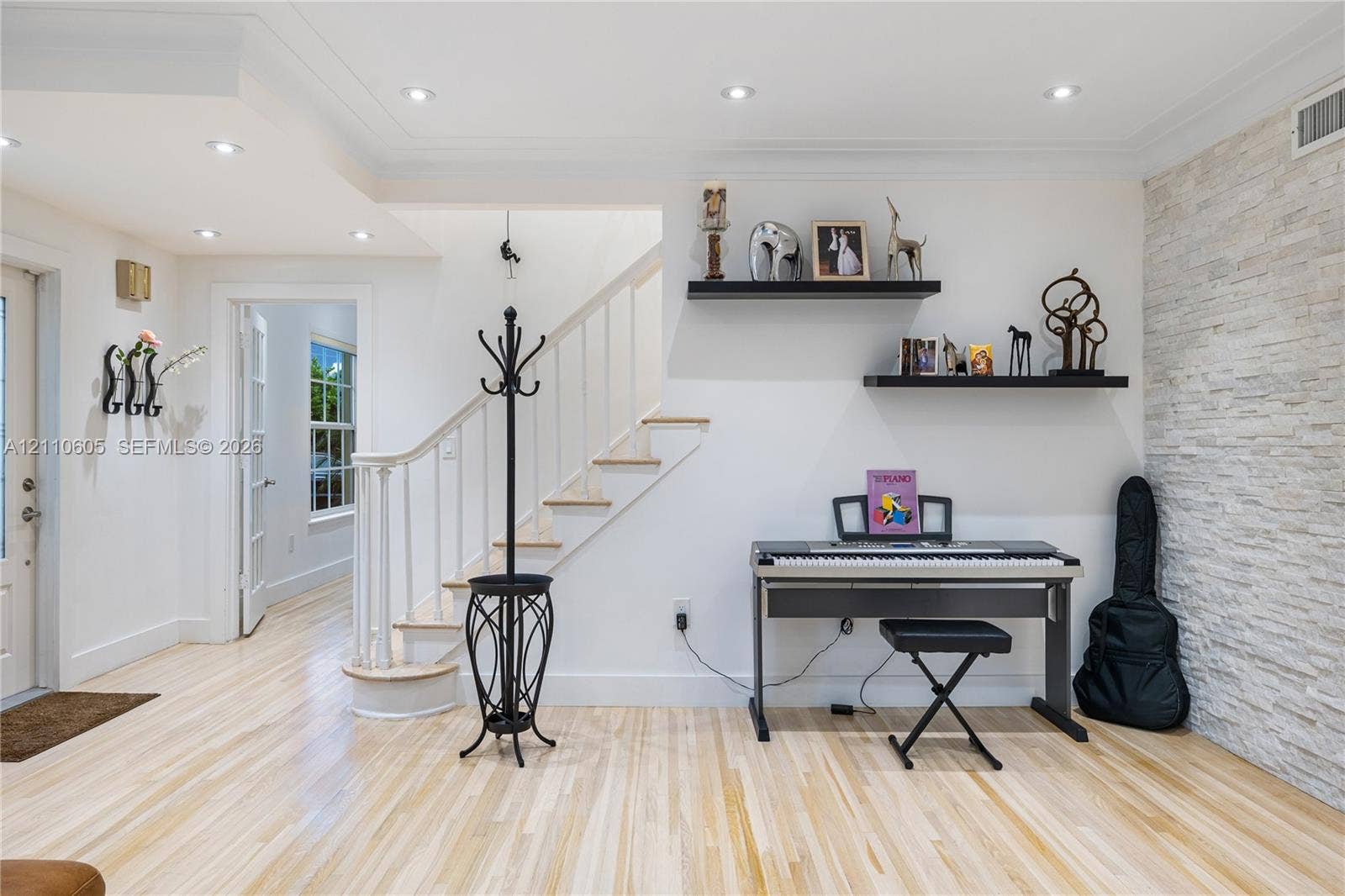 Light wood-finish flooring, textured stone accent wall, recessed lighting, and a staircase with a wooden handrail and balusters