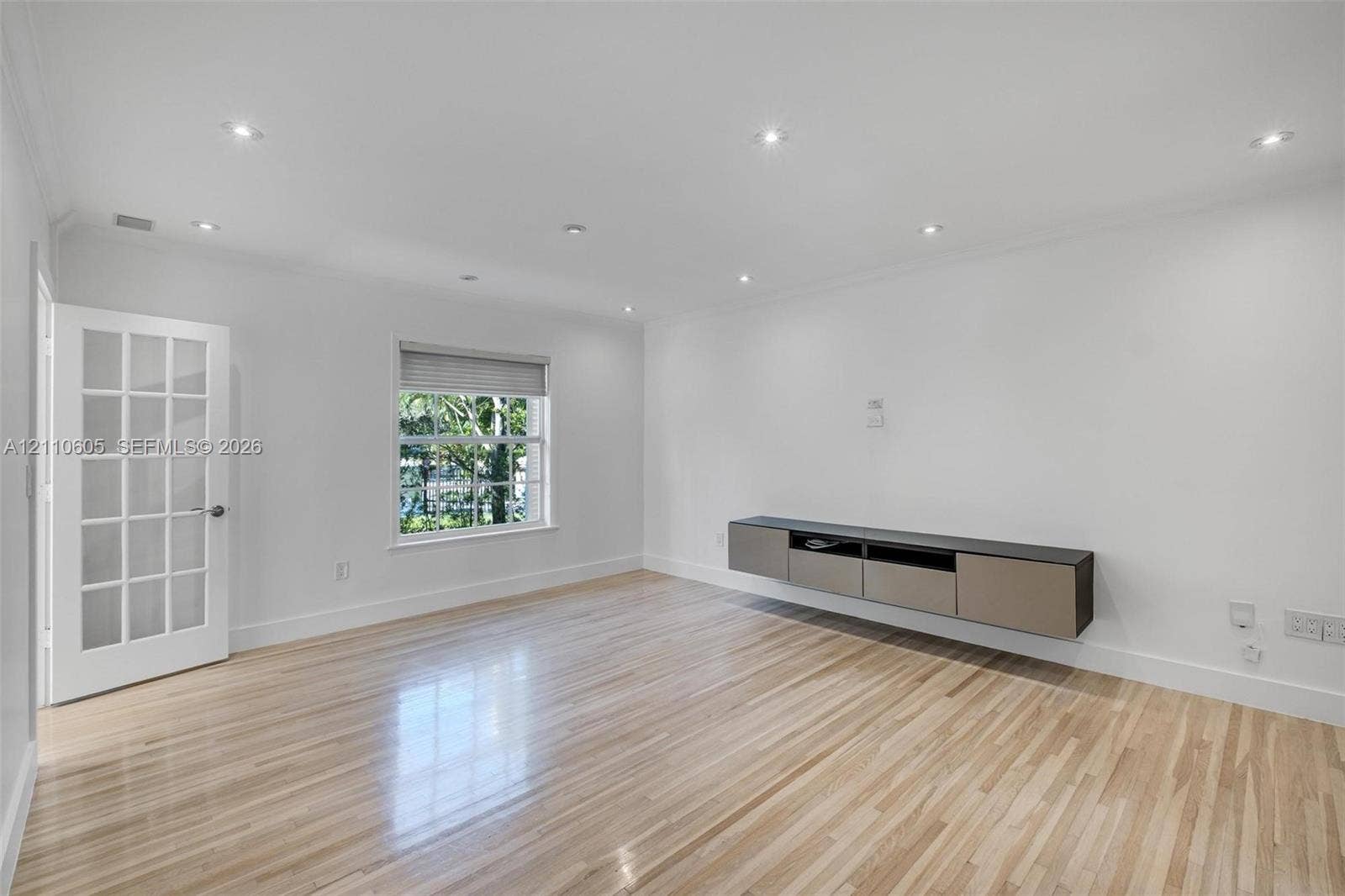 Light-filled room featuring wood-finish flooring, a floating wall-mounted cabinet, recessed lighting, and a multi-pane glass-panel door