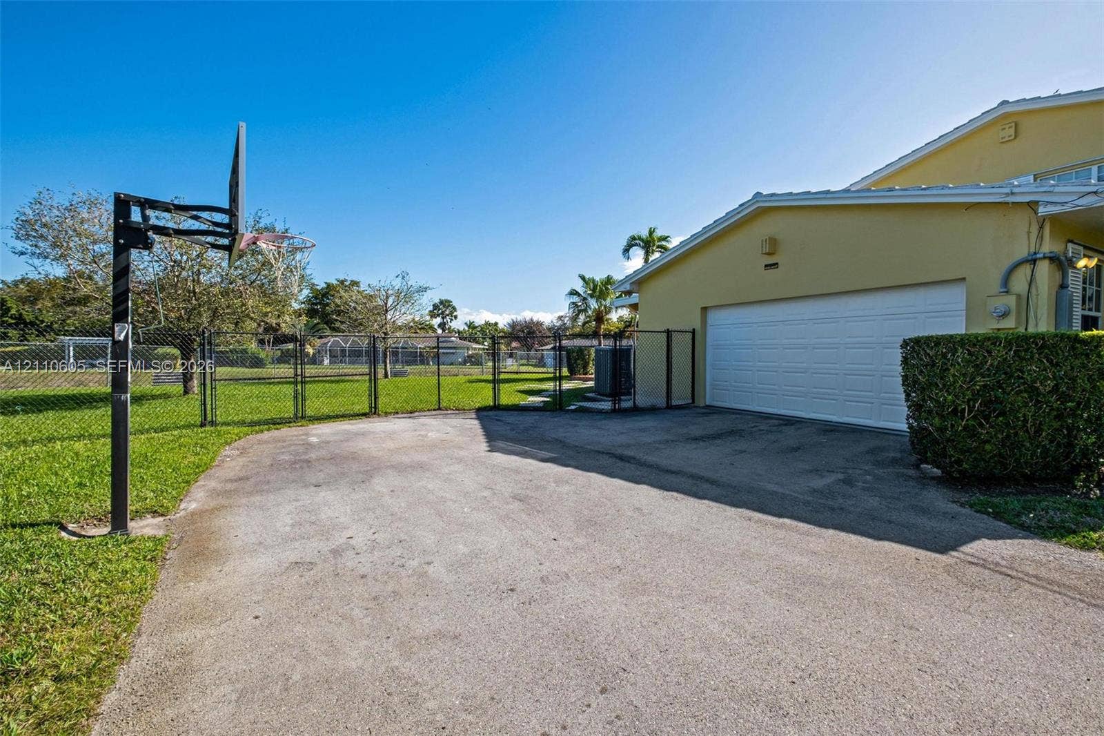 Asphalt driveway, attached two-car garage with white sectional door, chain-link perimeter fencing, and open outdoor recreational space