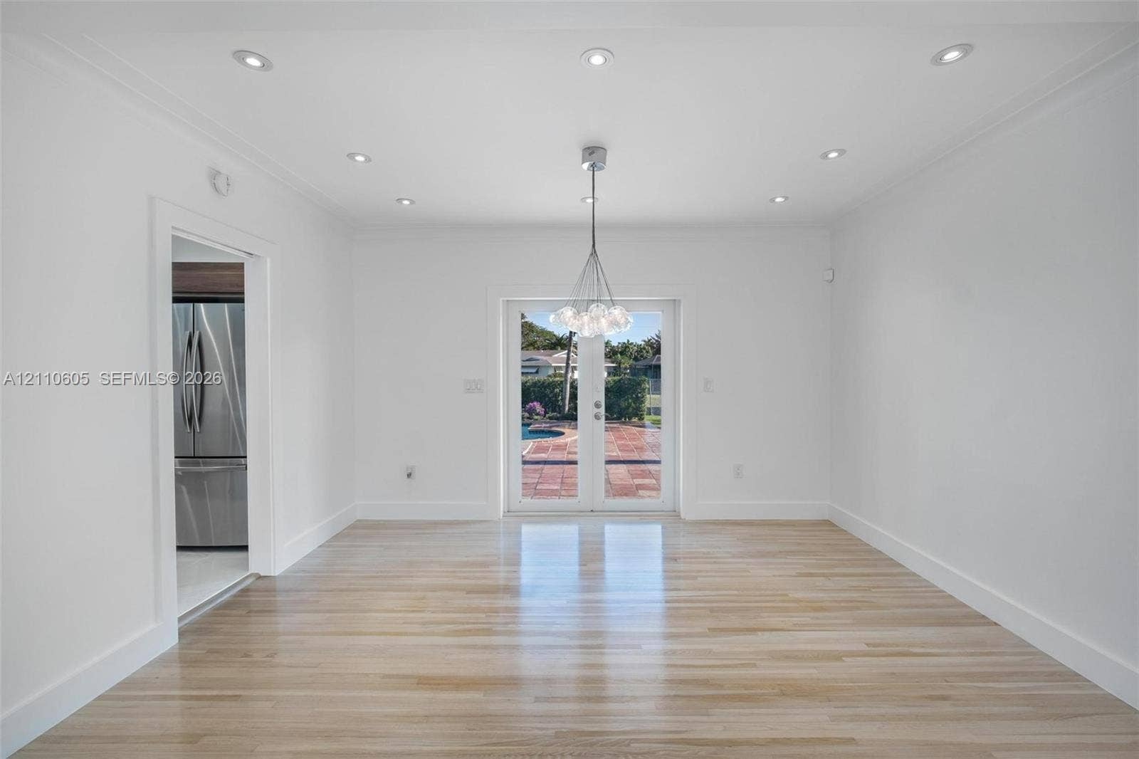 Open-concept area featuring light wood-finish flooring, recessed lighting, a multi-bulb glass pendant fixture, and glass-paneled double doors