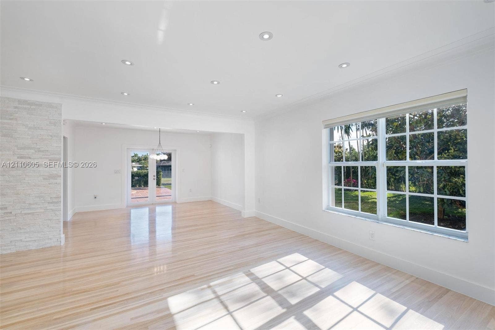 Light-filled interior featuring wood-finish flooring, recessed lighting, a stone-textured accent wall, multi-pane windows, and glass-paned double doors