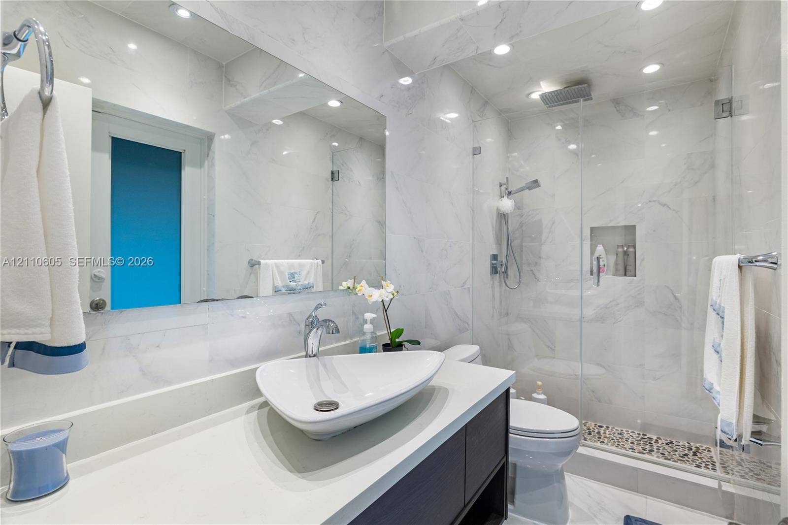 Bathroom featuring full-height stone-finish wall tile, frameless glass shower enclosure, recessed shower niche, vessel sink with chrome hardware, and integrated vanity cabinetry